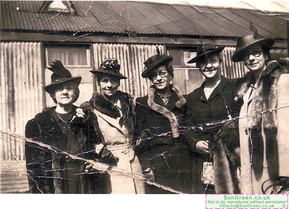 A group of ladies outside a tin hut.